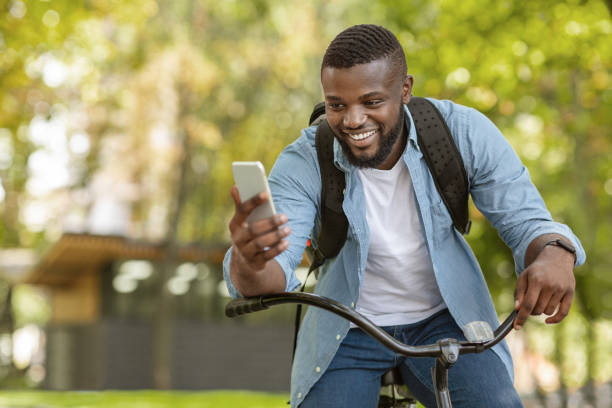 istock Happy Black Man Riding Bicycle Outdoors And Using Smartphone 1210745261