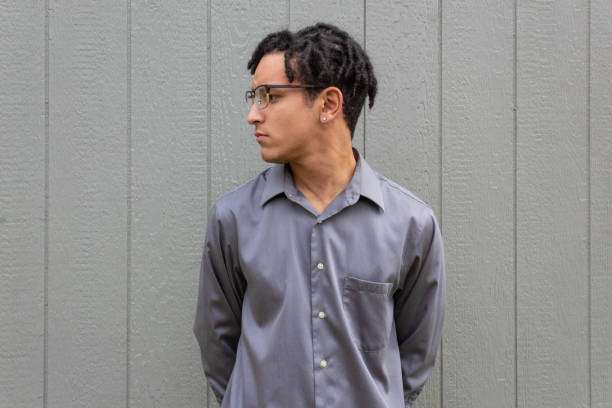 Young black man in profile, collared shirt with hands behind back, pensive look, natural black hair in twists
