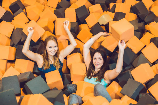 deux jeunes femmes s’amusant avec des blocs mous à l’aire de jeux intérieures d’enfants dans la fosse en caoutchouc de mousse dans le centre de trampoline - building block photos et images de collection