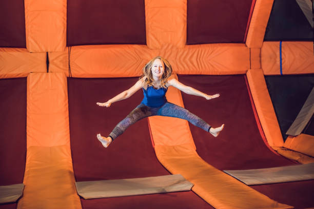 Young woman sportsman jumping on a trampoline in fitness park and doing exersice indoors Young woman sportsman jumping on a trampoline in fitness park and doing exersice indoors. trampoline stock pictures, royalty-free photos & images