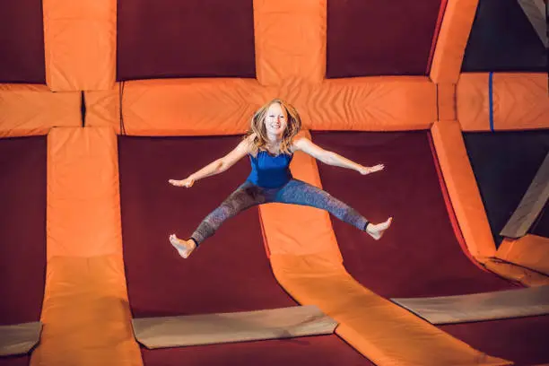 Young woman sportsman jumping on a trampoline in fitness park and doing exersice indoors.