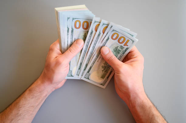 istock men's hands hold and count 100 dollar bills on gray background 1210745476