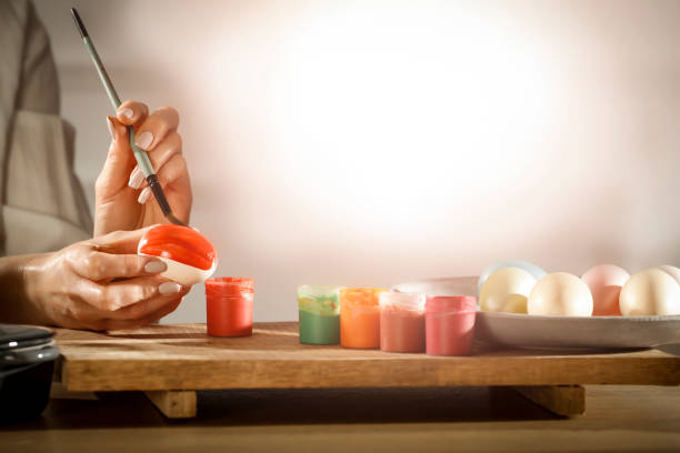 Female hands painting Easter eggs on wooden table on a spring day. Easter decoration time. Colorful eggs and paints on wooden board.