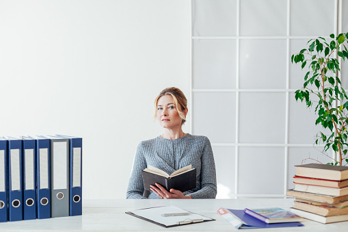 woman in business suit at the desk at work in the office with books