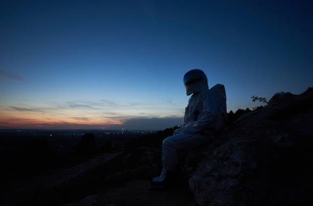 istock Astronaut sitting on rocky hill during sunset. 1210750192