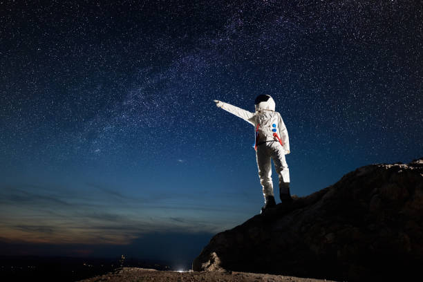 istock Astronaut standing on rocky mountain under night starry sky. 1210750212