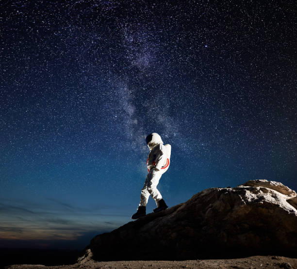 Space traveler walking down the mountain under starry sky. Full length of astronaut walking down the rocky hill under fantastic night sky with stars. Cosmonaut in space suit exploring the surface of new planet. Concept of galaxy, milky way and space travel. spacewalk photos stock pictures, royalty-free photos & images