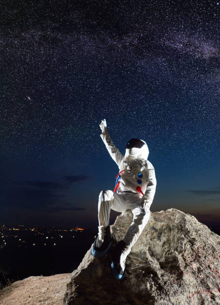 istock Spaceman sitting on rocky mountain and pointing at stars. 1210750274