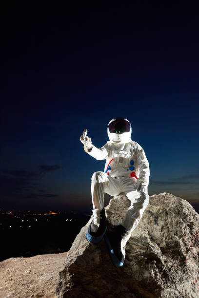 istock Spaceman sitting on rocky mountain and showing middle finger. 1210750309