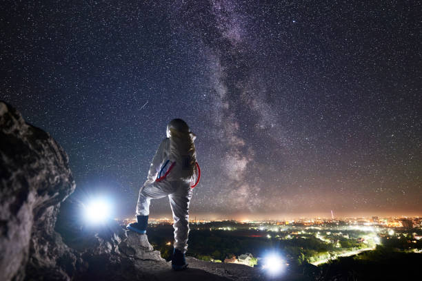 istock Cosmonaut standing on rocky hill and looking at night sky. 1210750375