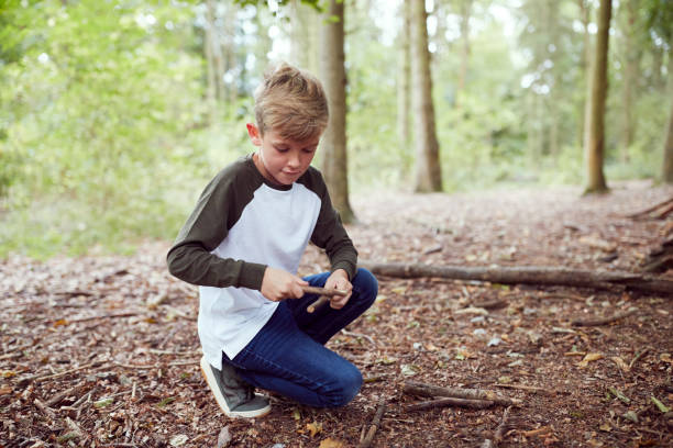 istock Boy On Outdoor Camping Trip In Forest Learning How To Make Fire By Rubbing Sticks Together 1210750567