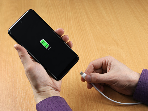 Man disconnect the charging cable from the smartphone. Full charge visible on screen