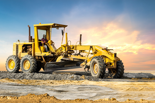 Industrial motor grader on ground in sunset background, earth moving engine equipment