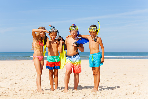 Group of kids with scuba snorkeling masks fins in swimwear stand near the sea