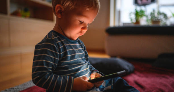 istock Cute boy holding mobile phone and sitting on the floor 1210759450