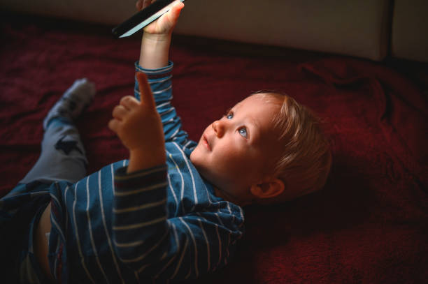 istock Cute boy holding mobile phone and lying on back on the floor 1210759464