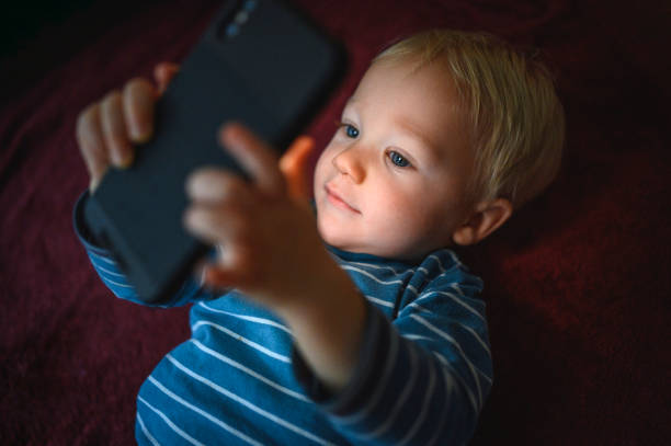 istock Cute boy holding mobile phone and lying on back on the floor 1210759473