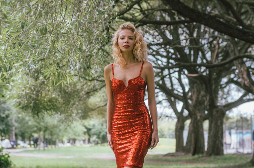 Portrait of beautiful blond girl in red short dress with sequins in park