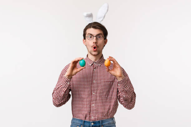 traditions, religious holidays, celebration concept. amused enthusiastic handsome young man suggest girlfriend play easter game on family gathering party, hold two painted eggs, wear rabbit ears - mask religious celebration horizontal easter imagens e fotografias de stock