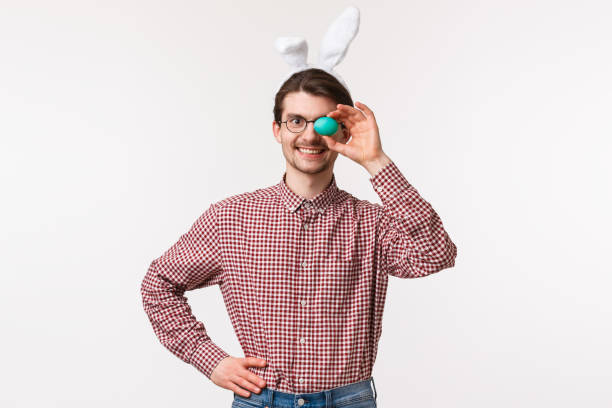 traditions, religious holidays, celebration concept. waist-up portrait of cheerful funny caucasian man in rabbit ears, holding one painted egg and smiling satisfied, prepared easter day meal - mask religious celebration horizontal easter imagens e fotografias de stock