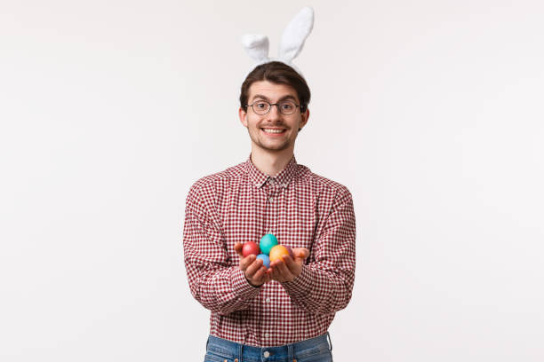 traditions, religious holidays, celebration concept. lovely and caring adult man in glasses and rabbit ears, holding painted eggs and smiling, give it to person and congratulate with happy easter day - mask religious celebration horizontal easter imagens e fotografias de stock