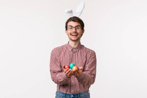 traditions, fêtes religieuses, concept de célébration. homme chrétien mignon amical et gai, portez des oreilles de lapin, retenant les oeufs de pâques peints et souriant joyeusement, félicitant avec le jour de bénédiction - easter bonnets photos photos et images de collection