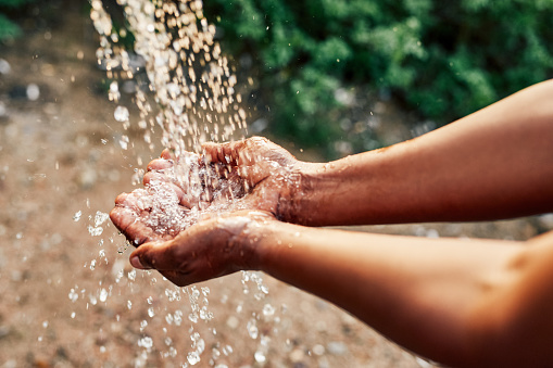 Cropped shot of an unrecognizable woman’s hands under a stream of running water outdoors