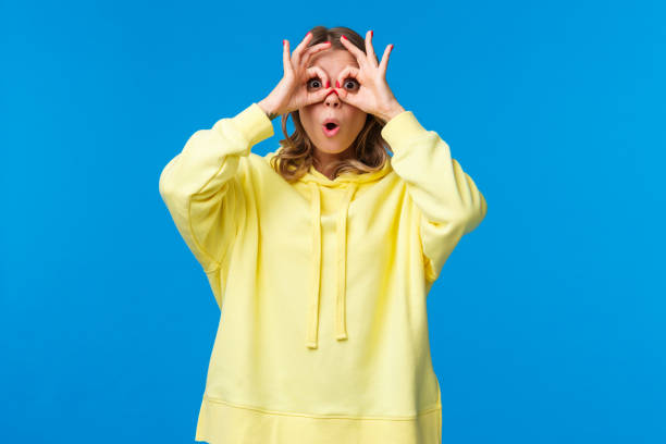 istock Wow interesting. Intrigued and surprised curious blond girl seeing something intriguing, open mouth astonished, look through hand-glasses and standing blue background 1210773343