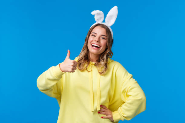 istock Holidays, traditions and celebration concept. Optimistic cute blond girl with rabbit ears laughing and showing approval gesture, thumb-up praise nice work, happy Easter, blue background 1210773801