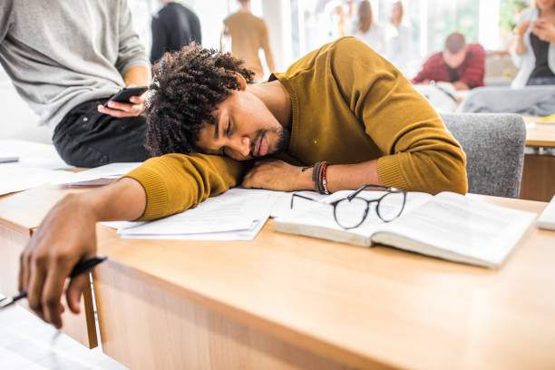Tired male student sleeping on a class in the classroom. Exhausted African American student taking a nap during a class in the classroom. male college student sleeping through lecture stock pictures, royalty-free photos & images