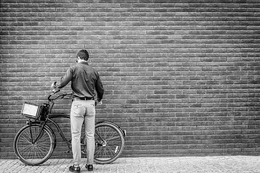 rear view on businessman leaning bicycle at brick wall