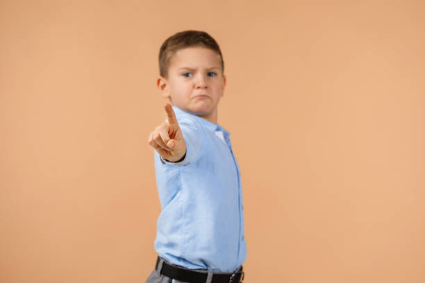 Cute little boy in shirt pointing camera on beige background. child pointing at you. focus on hand