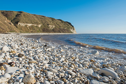 Landscape coastal scene of large stony pebble beach with chalks cliffs coastline dropping into sea