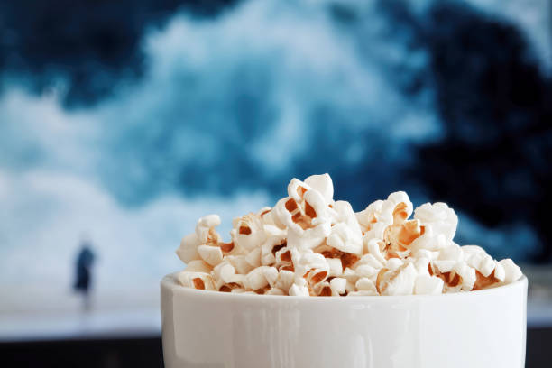 映画が再生されているテレビ画面に対するポップコーンでいっぱいのボウル - popcorn snack bowl corn ストックフォトと画像