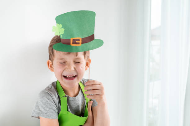 concepto de vacaciones del día de san patricio. alegre emocional chico rubio caucásico con papel verde sombrero duende con trébol sobre fondo blanco - st patricks day irish culture child leprechaun fotografías e imágenes de stock