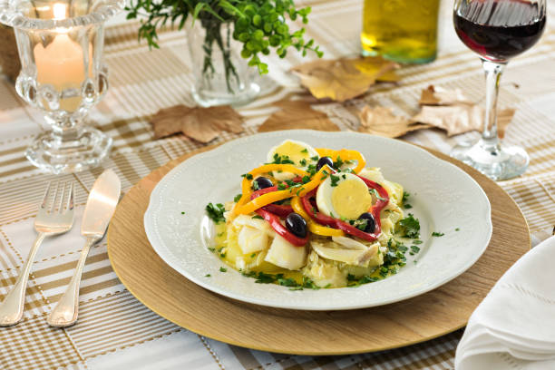 A codfish with bell pepper, boiled egg, black olives and parsley Table set for a dinner, with white decorated portuguese plate. A codfish with bell pepper, boiled egg, black olives and parsley is being served, an typical portuguese dish. fusion food photos stock pictures, royalty-free photos & images