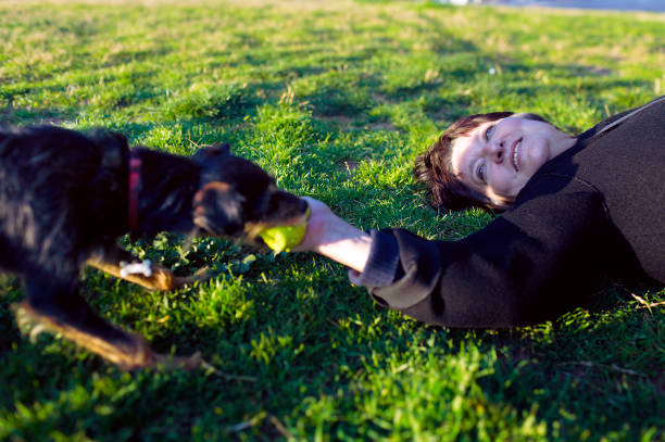 istock Mature woman lying on the grass playing with her dog 1210799376