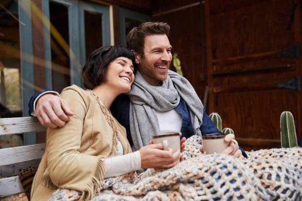 Laughing couple drinking coffee on a bench outside on a cool morning