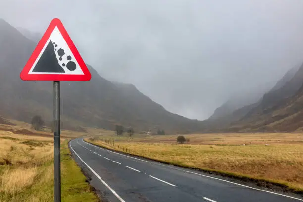 A sign warning of danger of landslides and falling rock on the road through Glencoe in Scotland, during heavy rain.