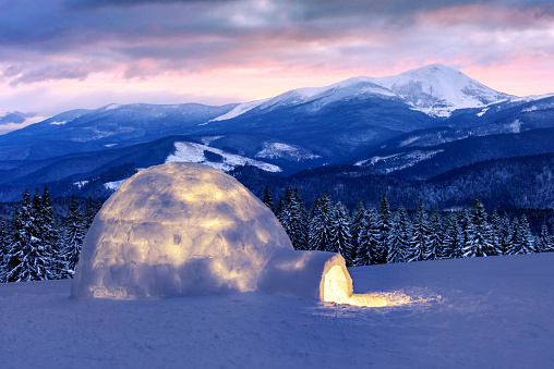 Real snow igloo house in the winter mountains. Snow-covered firs and mountain peaks on the background. Foggy forest with snowy spruce