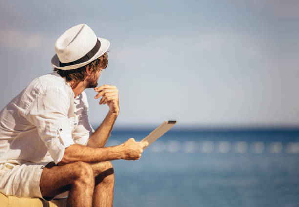 istock Man relaxing and use tablet computer at sea beach 1210806045