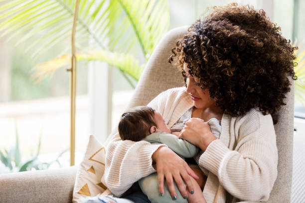 New mother breastfeeds baby in living room of home The new mid adult mother sits comfortably in a chair in her living room and breastfeeds her baby. breastfeeding photos stock pictures, royalty-free photos & images