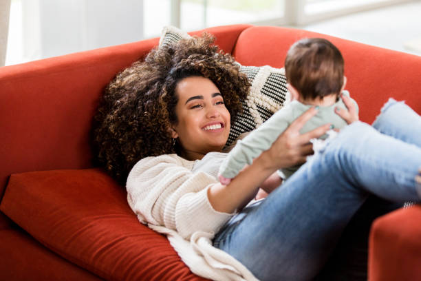 istock Mom lying on couch holds baby up in lap 1210806673