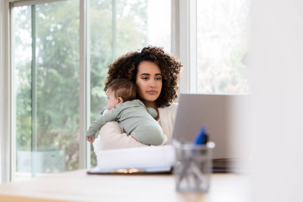 istock Stay-at-home mom holds baby while working remote 1210807917