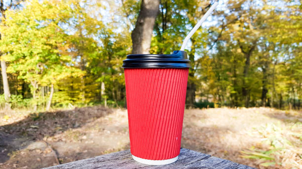 istock a red corrugated paper cup with coffee covered with a brown lid and a white drinking straw stands in the forest on a gray wooden table against the background of nature and trees. Copy space 1210808213