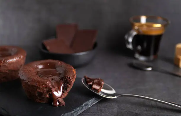Homemade chocolate lava cake on a black plate with a coffee on a black background