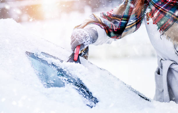 フロントガラスから雪を掃除する女性、凍った氷のガラスを削る。冬の車のクリーンフロントウィンドウ - snow car window ice scraper ストックフォトと画像