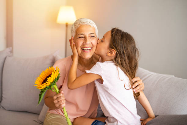 Celebrating mothers day or 8 march concept Little preschool granddaughter kissing happy older grandma on cheek giving violet flowers bouquet congratulating smiling senior grandmother with birthday, celebrating mothers day or 8 march concept kissing photos stock pictures, royalty-free photos & images