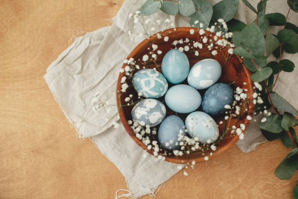 istock Happy Easter flat lay. Modern Easter eggs in wooden bowl with spring flowers and eucalyptus on rustic table. Stylish pastel blue Easter eggs painted in natural dye from red cabbage. 1210817333