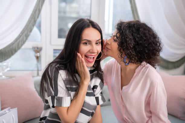istock Two dark-haired women sitting on the sofa and sharing secrets 1210820007